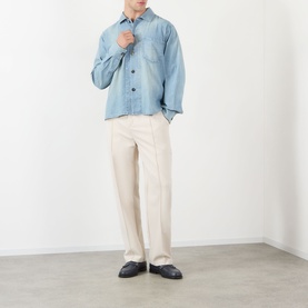Model wearing JW Anderson Slant Pocket Denim Shirt in pale blue with pointed collar and washed effect, styled with cream wide-leg trousers and black