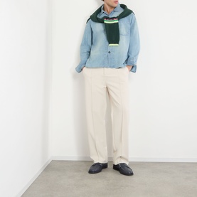 Model wearing JW Anderson Slant Pocket Denim Shirt in pale blue with cream trousers, green scarf, and dark loafers.