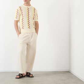 Model wearing JW Anderson Chevron Pattern Sweater in ivory with multicolour zigzag knit, paired with cream wide-leg trousers and black sandals.