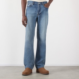 Model wearing JW Anderson Mid-Rise Straight Leg Jeans in mid blue faded wash with five-pocket styling, paired with tan suede shoes.