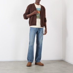 Model wearing JW Anderson Mid-Rise Straight Leg Jeans in mid blue faded wash, styled with brown cardigan, graphic tee and suede boots.