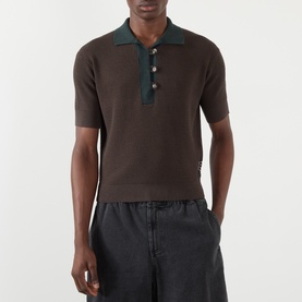 Model wearing JW Anderson Military Green cotton-cashmere polo with contrast collar and buttons, styled with dark grey trousers.