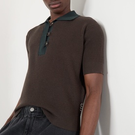 Model wearing JW Anderson Military Green cotton-cashmere knit polo with contrast collar and gold-tone buttons, styled with dark jeans