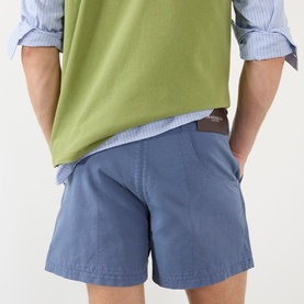 Model wearing JW Anderson Hiking Chino Shorts in steel blue cotton with belt loops, shown from back with hands in pockets, styled with green tee and