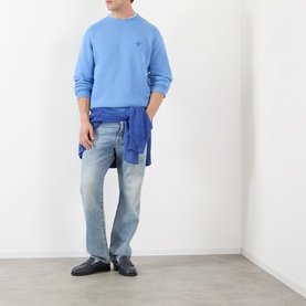 Model wearing JW Anderson Ribbon Anchor Logo Sweatshirt in washed blue, styled with light-wash jeans and a blue shirt tied at the waist.