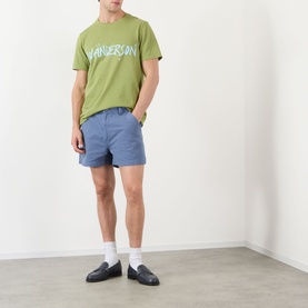 Model wearing JW Anderson Circular Logo T-Shirt in leaf green with blue shorts and black loafers.