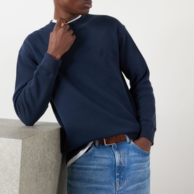Model wearing JW Anderson navy cotton sweatshirt with anchor embroidery, styled with light wash jeans and brown leather belt.