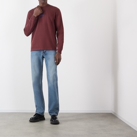 Model wearing JW Anderson burgundy long-sleeve cotton T-shirt with light wash straight-leg jeans and black loafers