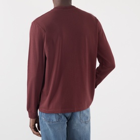Model wearing JW Anderson burgundy long-sleeve cotton T-shirt, back view, styled with light blue jeans.