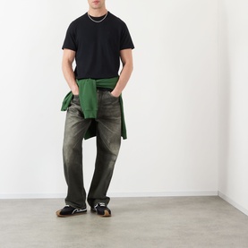 Model wearing JW Anderson Anchor Logo T-Shirt in black with faded jeans, green shirt tied at waist, and black sandals.