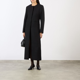 Model wearing Loulou Studio black wool blend longline coat with collarless neckline, styled with black bag and heeled boots