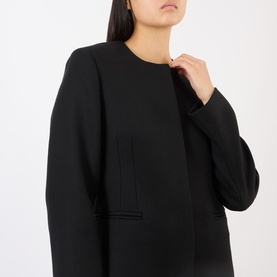 Model wearing Loulou Studio black wool coat with collarless neckline, long sleeves, and front patch pockets