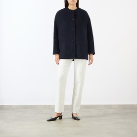 Model wearing Loulou Studio navy melange wool-cashmere coat with collarless neckline and button front, styled with white trousers and black mules.