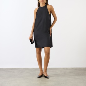 Model wearing Loulou Studio black silk dress with halterneck silhouette, styled with black clutch and flat pointed-toe shoes