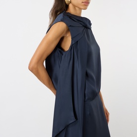 Model wearing Loulou Studio navy silk dress with draped bow neckline and sleeveless cut, styled with gold earrings