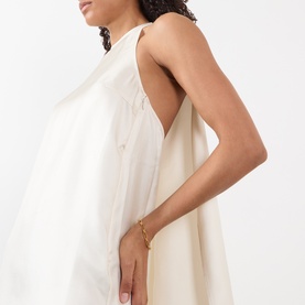 Model wearing Loulou Studio ivory silk dress, sleeveless A-line silhouette with draped back detail, styled with a gold chain bracelet.