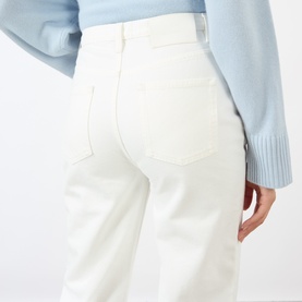 Model wearing Loulou Studio ivory high-waist jeans, rear view, styled with a light blue knit sweater.