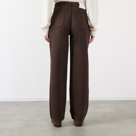 Model wearing Loulou Studio brown wide-leg jeans, rear view, styled with a cream knit top and brown boots.
