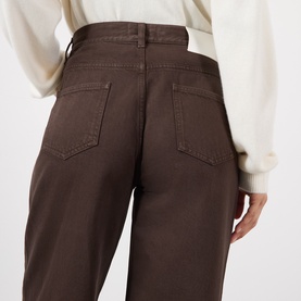 Model wearing Loulou Studio brown cotton jeans, rear view showing high waist and back pockets, styled with a cream knit top.