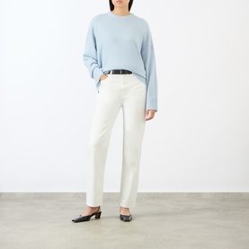 Model wearing Loulou Studio light blue cashmere knit sweater with cream straight-leg jeans, black belt, and black mules.