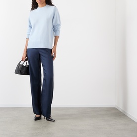 Model wearing Loulou Studio Baltra Knitted Sweater in light blue cashmere with crew neck, styled with navy wide-leg trousers and black heels