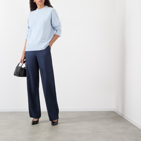 Model wearing Loulou Studio Baltra Knitted Sweater in light blue cashmere with crew neck, styled with navy wide-leg trousers and black heels.