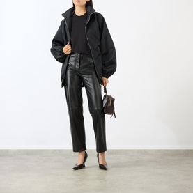 Model carrying small dark brown structured bag, styled with black oversized zip jacket, faux leather trousers and black pointed-toe heels