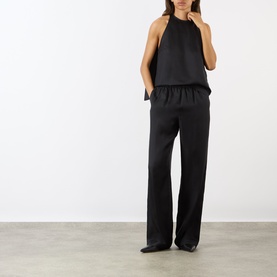 Model wearing Loulou Studio Cami Silk Cape Top in black, styled with matching black wide-leg trousers and black pointed-toe flats.