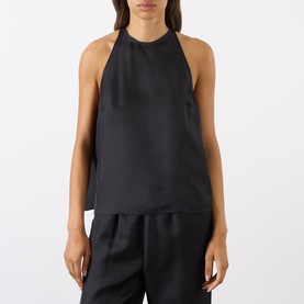 Model wearing Loulou Studio Cami Silk Cape Top in black, featuring halter neckline and sleeveless silhouette, styled with black wide-leg trousers