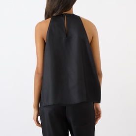 Model wearing Loulou Studio Cami Silk Cape Top in black, showing rear cape panel and teardrop cutout at neck. Styled with black trousers.
