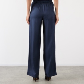 Model wearing Loulou Studio navy silk wide-leg trousers, shown from behind with elasticated waistband, styled with black heels.