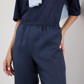 Model wearing Loulou Studio navy silk trousers with elasticated waist and side pocket, styled with a navy T-shirt and striped blue shirt.