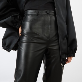 Model wearing Loulou Studio black lambskin leather trousers with high waist and straight leg, styled with matching black leather jacket.