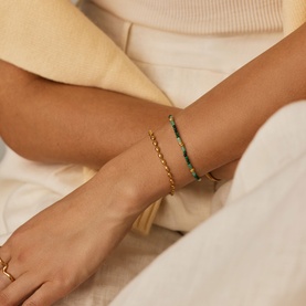 Model with Missoma bracelet stack in gold and green, featuring a gold chain and green beaded bracelet, worn together on wrist