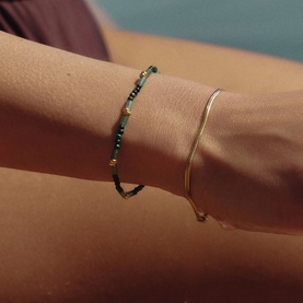 Model with Missoma bracelet in gold and green beaded design, styled with a gold snake chain bracelet on wrist