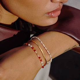 Model with Missoma gold and red bracelet stack, styled with pearl and crystal tennis bracelets on wrist.