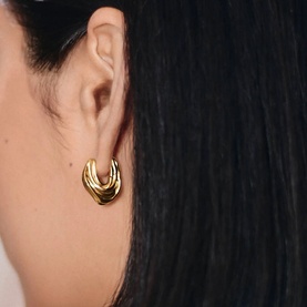 Model with Missoma gold chunky ridged hoop earrings, shown close up on ear against dark hair