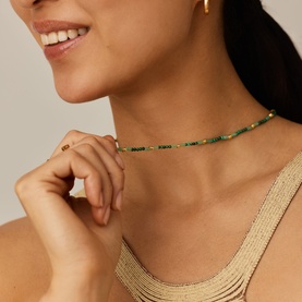 Model with Missoma gold and green beaded choker necklace, styled with a gold strappy top and small gold hoop earrings.