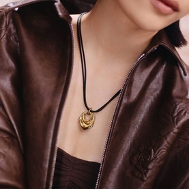 Model with Missoma gold cord necklace featuring a chunky gold interlocked pendant, styled with a brown leather jacket.