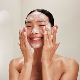 Model applying Rituals Gentle Cleansing Foam to face, smiling with eyes closed, white lather visible across cheeks and forehead