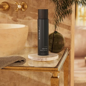 Rituals Homme Shave Foam in tall dark bottle displayed on marble dish beside stone basin and folded towel