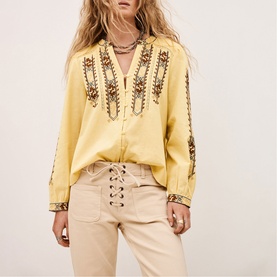 Model wearing Bash yellow embroidered boho blouse with V-neck, styled with beige lace-up trousers and layered necklaces.