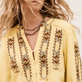 Model wearing Bash yellow top with brown embroidered detail at neckline, styled with layered beaded necklaces