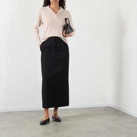 Model wearing Soeur light pink merino wool V-neck knit with black midi skirt and flat shoes, carrying a small black bag.