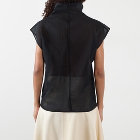 Model wearing Soeur black sleeveless top, rear view, showing mesh panel detail and high neck. Styled with cream wide-leg trousers.