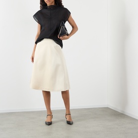 Model wearing Soeur black sleeveless top with mock neck, styled with cream midi skirt and black Mary Jane heels, carrying black clutch bag.