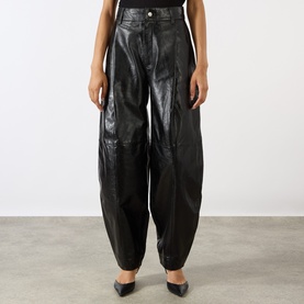Model wearing Soeur black lambskin leather wide-leg trousers with barrel silhouette, styled with black pointed-toe heels.