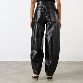 Model wearing Soeur black lambskin leather trousers, rear view, relaxed tapered fit with curved seam detailing, paired with black heels.