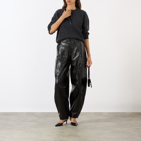 Model wearing Soeur black lambskin leather trousers with grey knit top and black heels, carrying a small black bag.