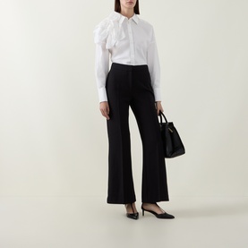 Model wearing Ted Baker black wide-leg trousers with a white ruffled shirt, black heels, and black tote bag.